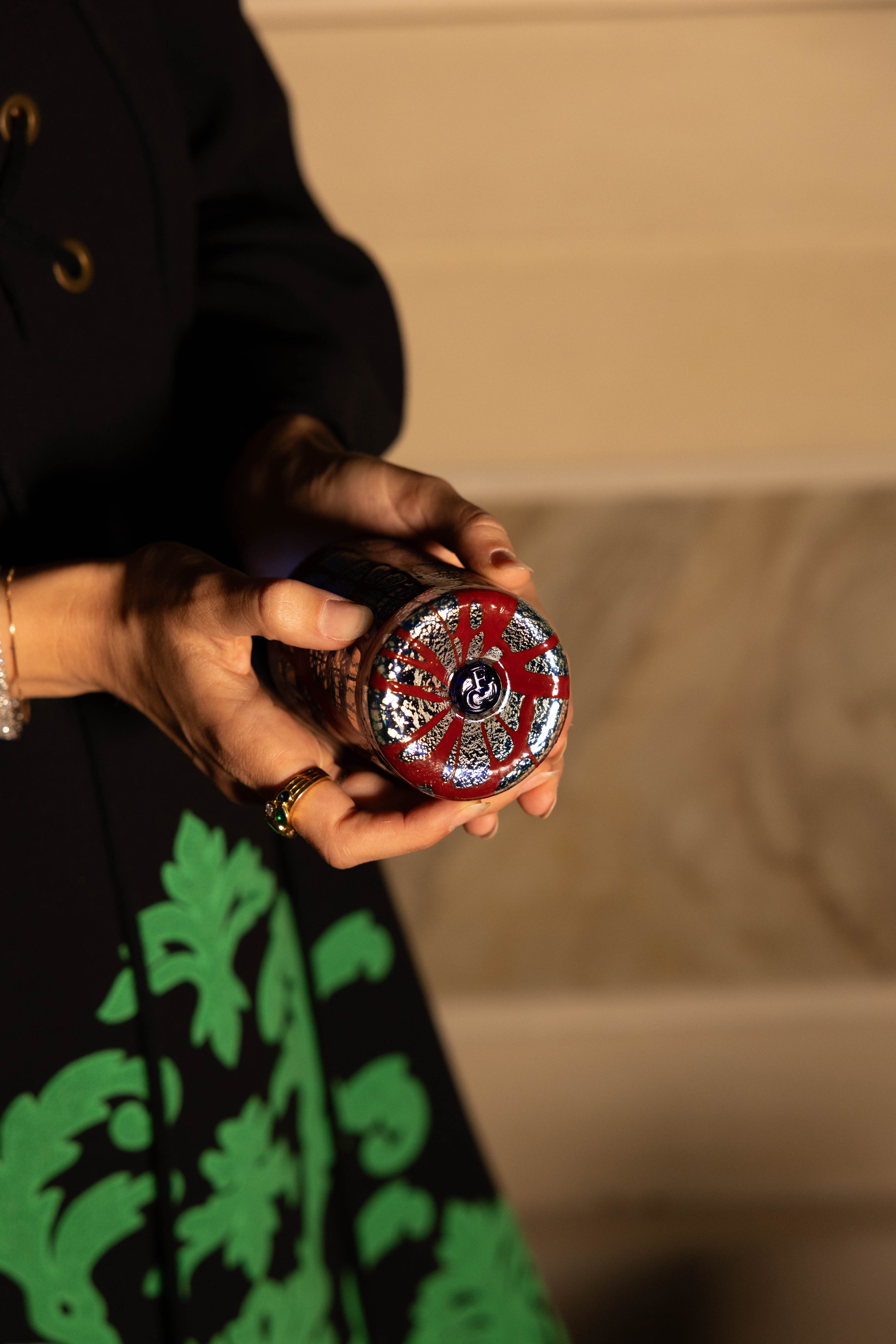 Woman wearing Gucci gown holding a hand-blown glass showing its details and logo featuring bordeaux enamel, silver leaf and hand crafted glass logo