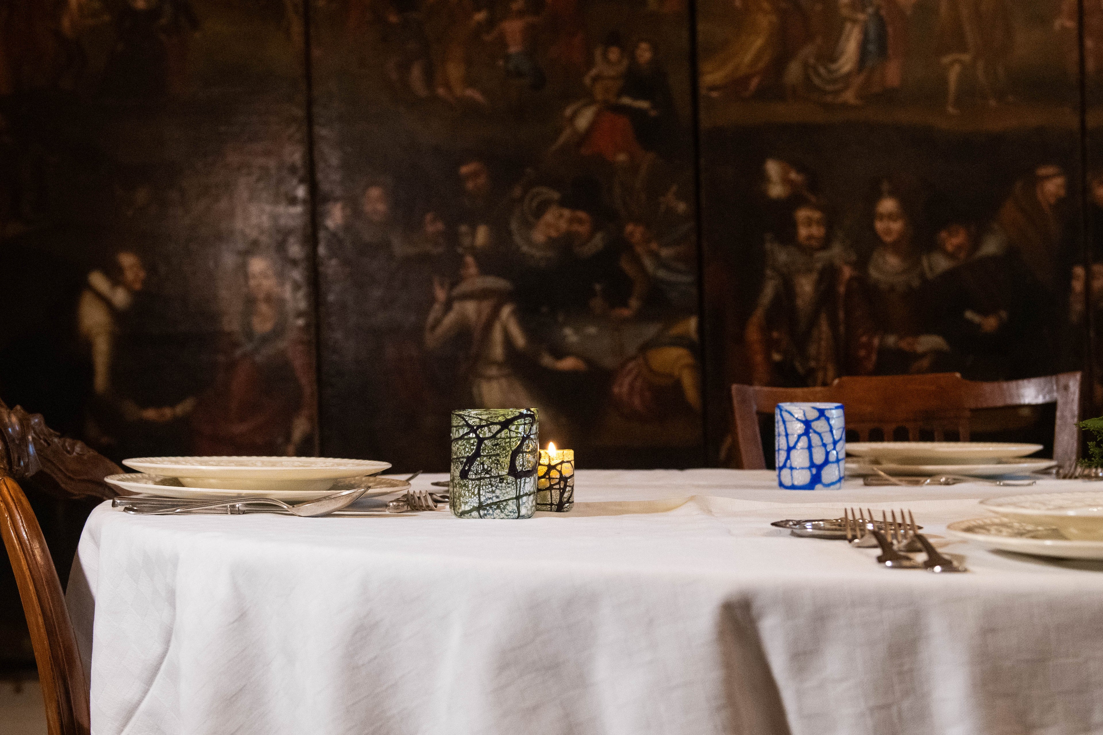 Dining table set with hand-blown glasses made in Venice and place cards candles against a historical painting backdrop